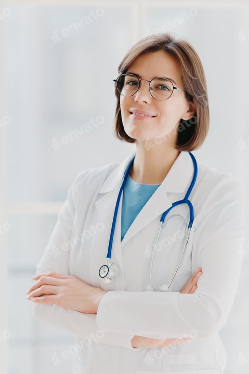 Preview: Female doctor wearing glasses and stethoscope standing with crossed arms in bright clinic office