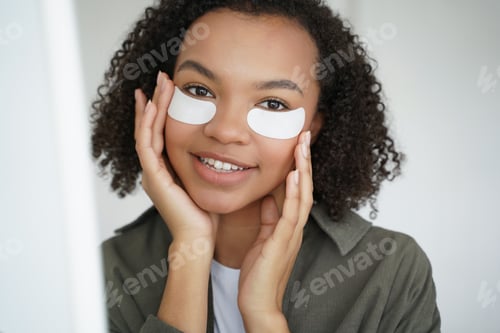 Preview: Smiling young African American woman with under eye patches touching face during skincare beauty rou