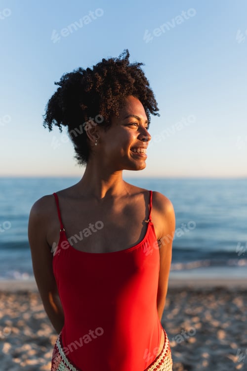 Preview: Smiling woman enjoying golden hour on beach vacation