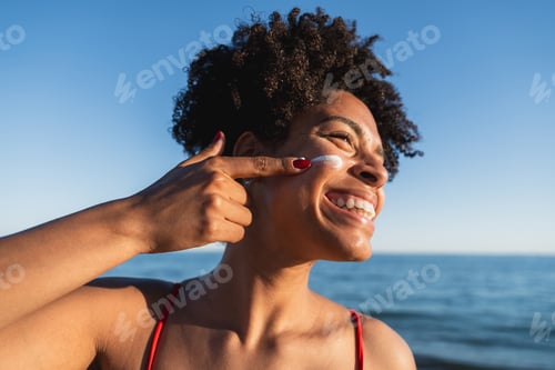 Preview: Happy woman applying sunscreen at beach during summer
