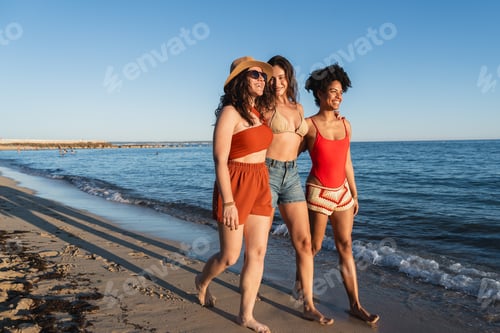 Preview: Three diverse women friends walking along beach enjoying summer