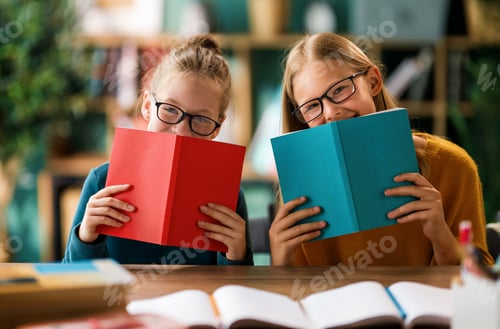 Two Young Girls Smiling While Hiding Behind Colorful Books