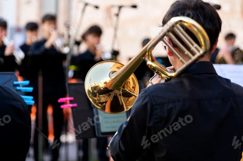 Preview: Young musician playing trombone with brass band in outdoor street concert