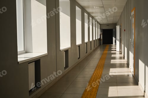 Preview: Sunlit school corridor with large windows and yellow tactile path on tiled floor,
