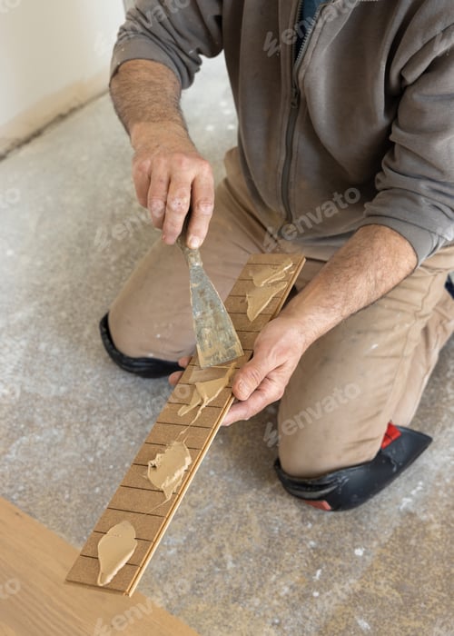 Preview: Construction worker applying adhesive on parquet planks during flooring installation in apartment