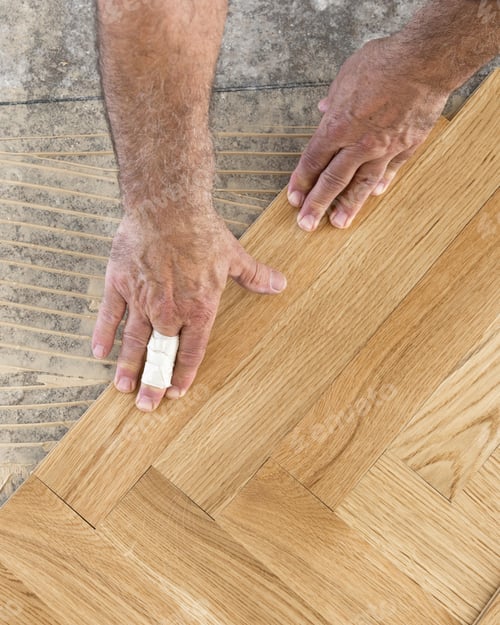 Preview: Hands installing herringbone wooden parquet planks during flooring work in apartment renovation
