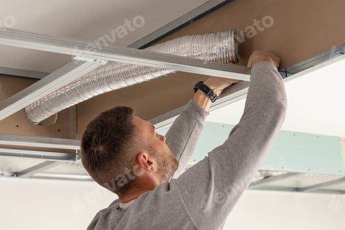 Preview: Construction worker handling metal profile frame in suspended ceiling system near flexible air duct