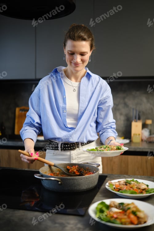 Preview: Woman cooks in modern kitchen while serving healthy food to plates during afternoon meal prep
