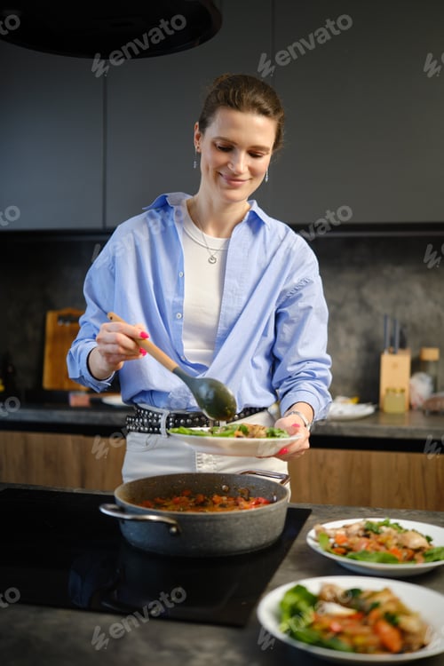 Preview: Woman serves meal in modern kitchen while smiling and enjoying cooking time with food
