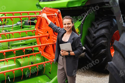 Preview: Businesswoman with a digital tablet presenting a new combine harvester at an agricultural equipment