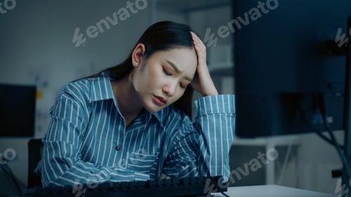 Preview: Stressed businesswoman feeling worried and fatigued while working overtime at computer in office at