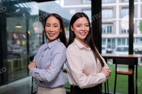 Preview: Asian businesswomen standing back to back. Smiling confidently. Showing partnership and teamwork wit