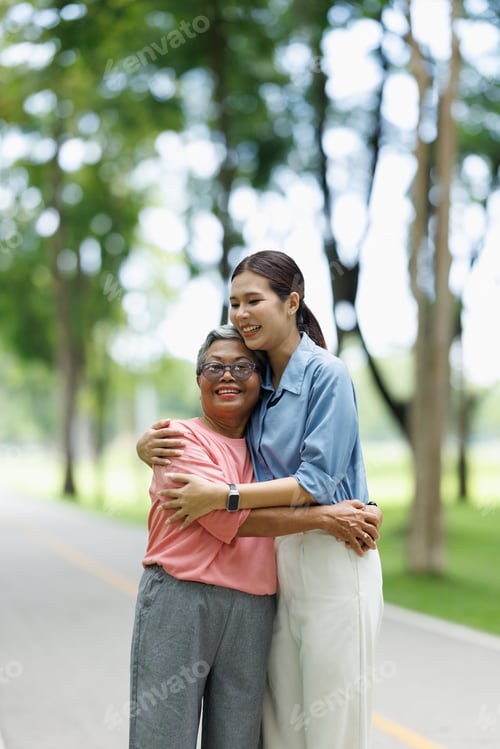 Preview: Two smiling asian women, an elderly mother and her adult daughter, hugging warmly in a green park, s