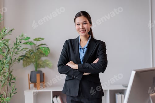 Preview: Smiling asian business woman wearing a headset and suit. Standing professionally with crossed arms.
