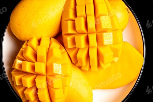 Preview: A close up arrangement of ripe yellow mango fruit sliced into cubes on a white plate.