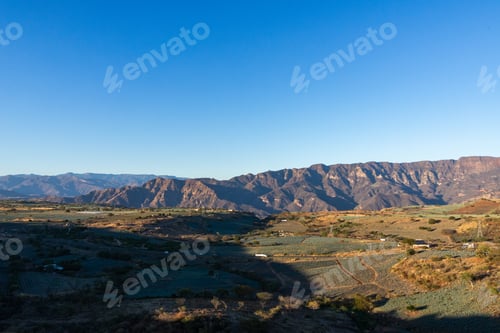 Preview: Serene Mountain Landscape with Rolling Hills and Agave Fields Under Clear Blue Sky