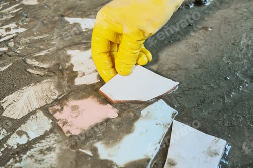 Preview: Hand in yellow rubber glove placing ceramic pieces into wet cement for mosaic. Upcycling old materia
