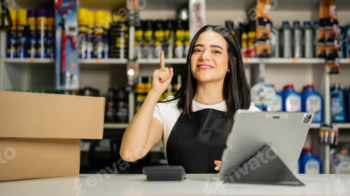 Preview: Smiling young woman pointing finger up, having a brilliant idea while working in an auto parts shop