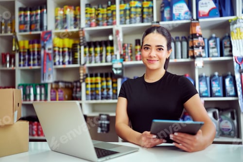 Preview: Young female entrepreneur smiling, using tablet and laptop in her automotive retail store
