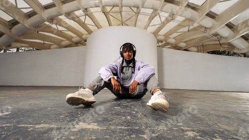 Preview: Young black woman relaxing on ground wearing headphones and streetwear