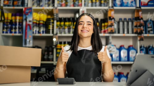 Preview: Smiling woman wearing an apron giving thumbs up inside an auto parts shop