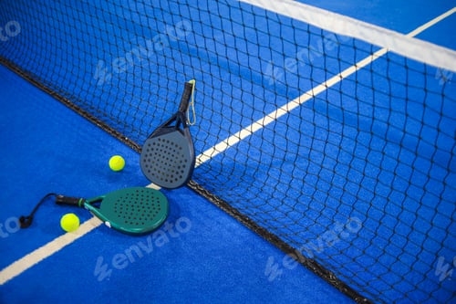 Preview: Two Padel Rackets And Two Balls Rest Near A Mesh Net On A Textured Court Surface