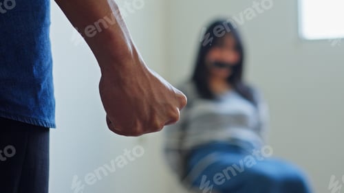 Preview: Criminal Clenches His Fist In The Foreground While A Scared Young Female Hostage Sits Gagged