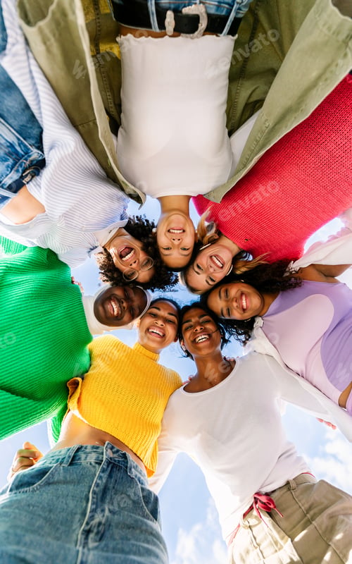 Preview: Group of diverse young women standing in a circle outdoors and looking down at camera.