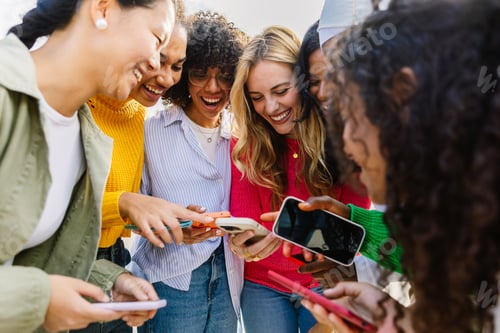 Preview: Group of female friends having fun using mobile phones outdoors.