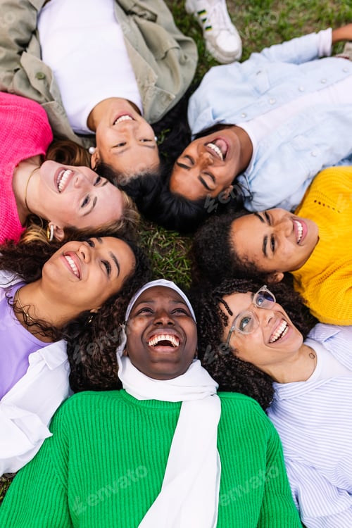 Preview: High angle view of diverse happy group of young girls lying on grass at park