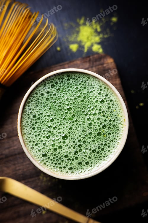 Preview: Close-up of matcha tea foam in a cup with bamboo whisk and spoon.