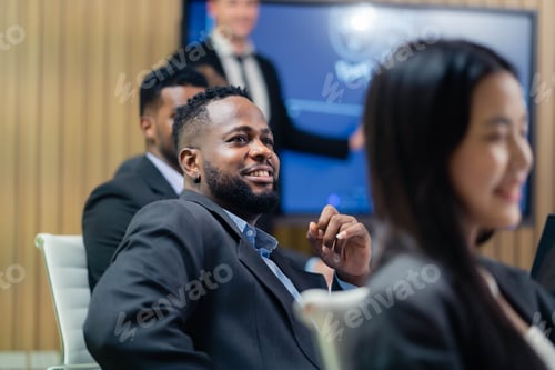 Preview: A man in a suit is smiling at a presentation. A woman is sitting next to him. The man is wearing a t