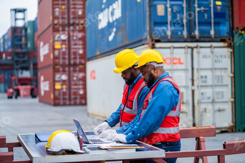 Preview: Two men in safety gear are working on a laptop in front of a container ship. Concept of productivity