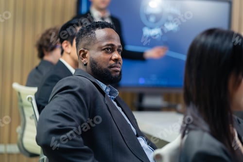 Preview: A man in a suit is smiling at a presentation. A woman is sitting next to him. The man is wearing a t