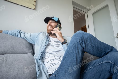 Preview: Joyful Man Talking on Smartphone While Relaxing on a Grey Sofa