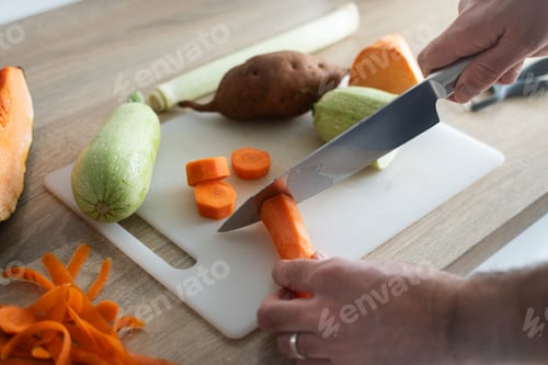 Preview: Cutting carrot on cutting board with fresh vegetables in kitchen