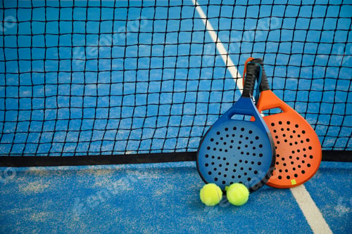 Preview: Padel rackets and balls are placed beside the net on court