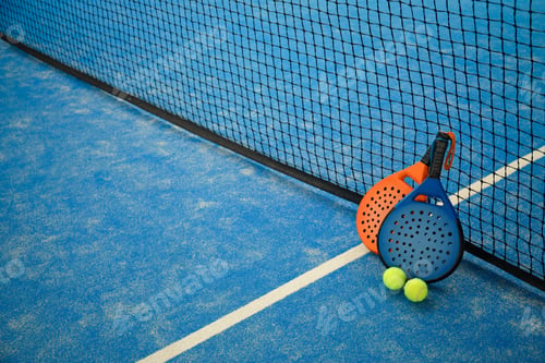 Preview: Padel rackets and balls rest on a blue court by the net