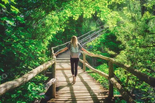Preview: Young woman walking on wooden boardwalk in green forest in summer