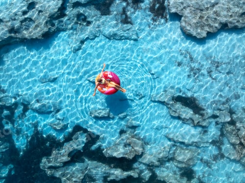 Preview: Aerialview of woman relaxing on pink inflatable ring in the sea