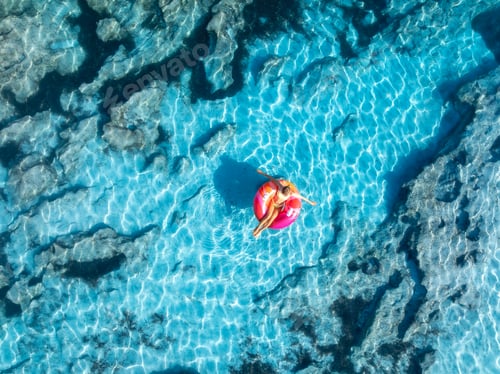 Preview: Aerial view of woman relaxing on pink inflatable ring in blue se
