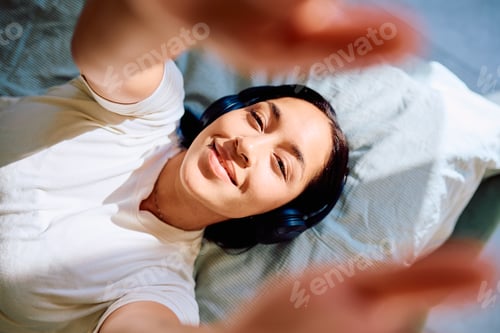 Preview: Young woman smiling while listening music in bed