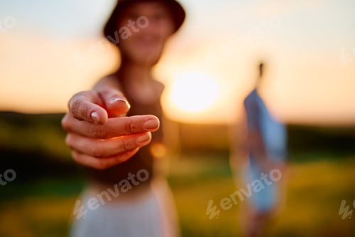 Preview: Woman extending hand inviting towards sunset
