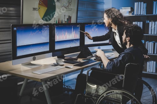 Preview: Professional man in wheelchair with thumbs up analyzing stock market graphs in office at night