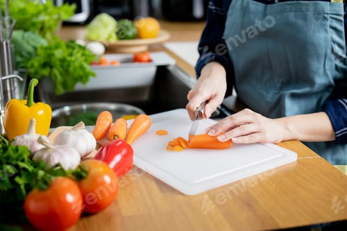 Preview: Happy young Asian woman cutting fresh vegetables in modern kitchen
