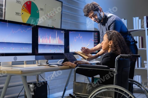 Preview: Diverse business team with woman in wheelchair analyzing financial data in night office