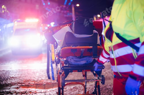 Preview: Paramedic Pulling Stretcher with Medical Equipment From Emergency Ambulance at Night