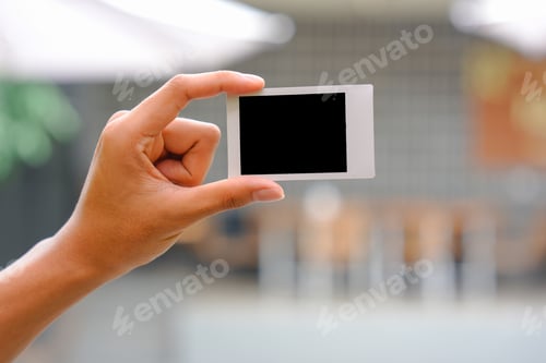 Preview: Close up of person's hand holding polaroid photo frame for mockup, outdoor nature background.