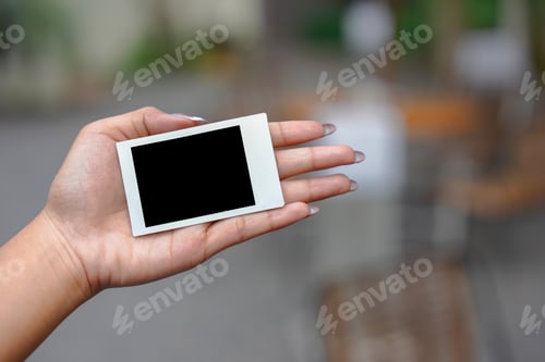 Preview: Close up of person's hand holding polaroid photo frame for mockup, outdoor nature background.