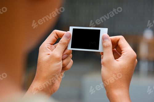 Preview: Close up of person's hand holding polaroid photo frame for mockup, outdoor nature background.